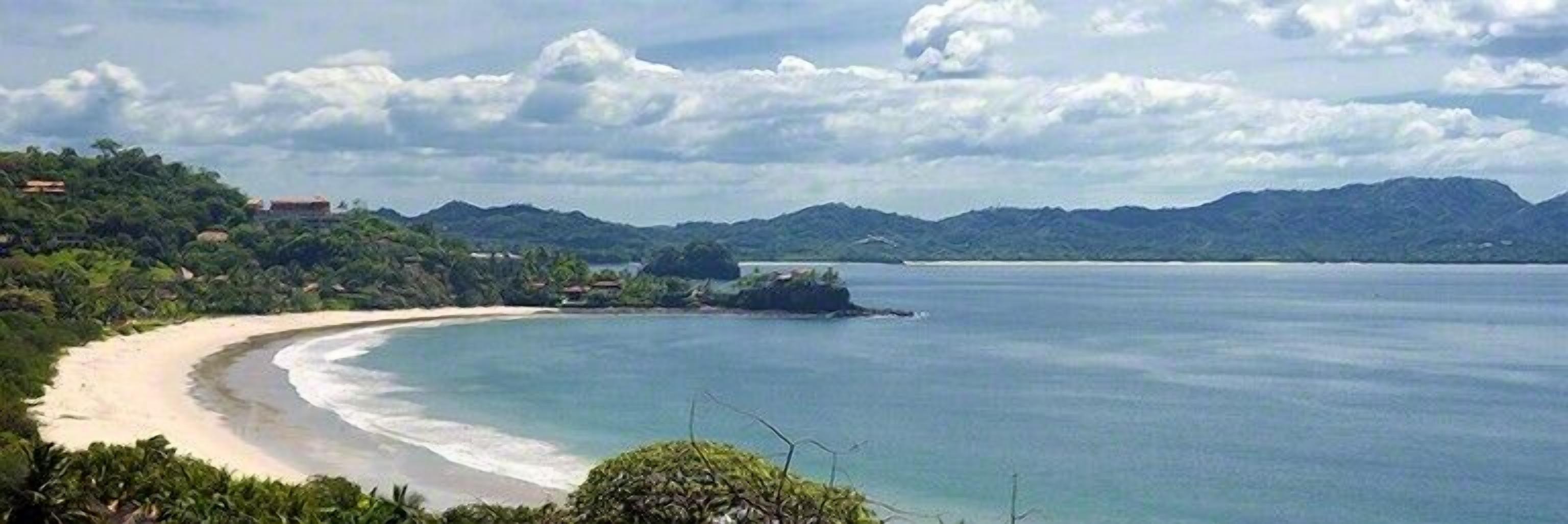 A coastal landscape with a sandy beach, a small island, and a mountain range in the background.