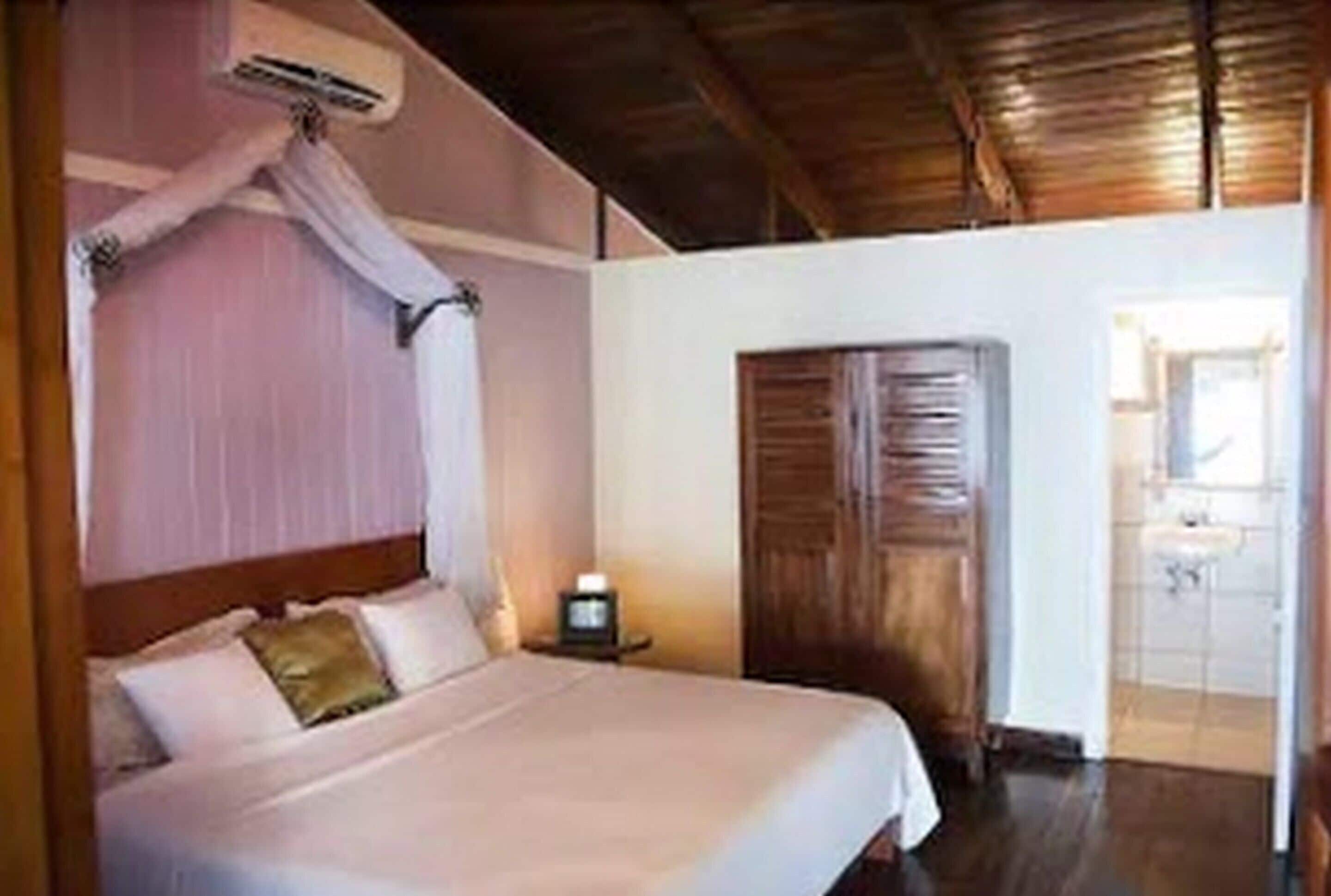 Quarto com cama, mesa de cabeceira e porta de madeira.