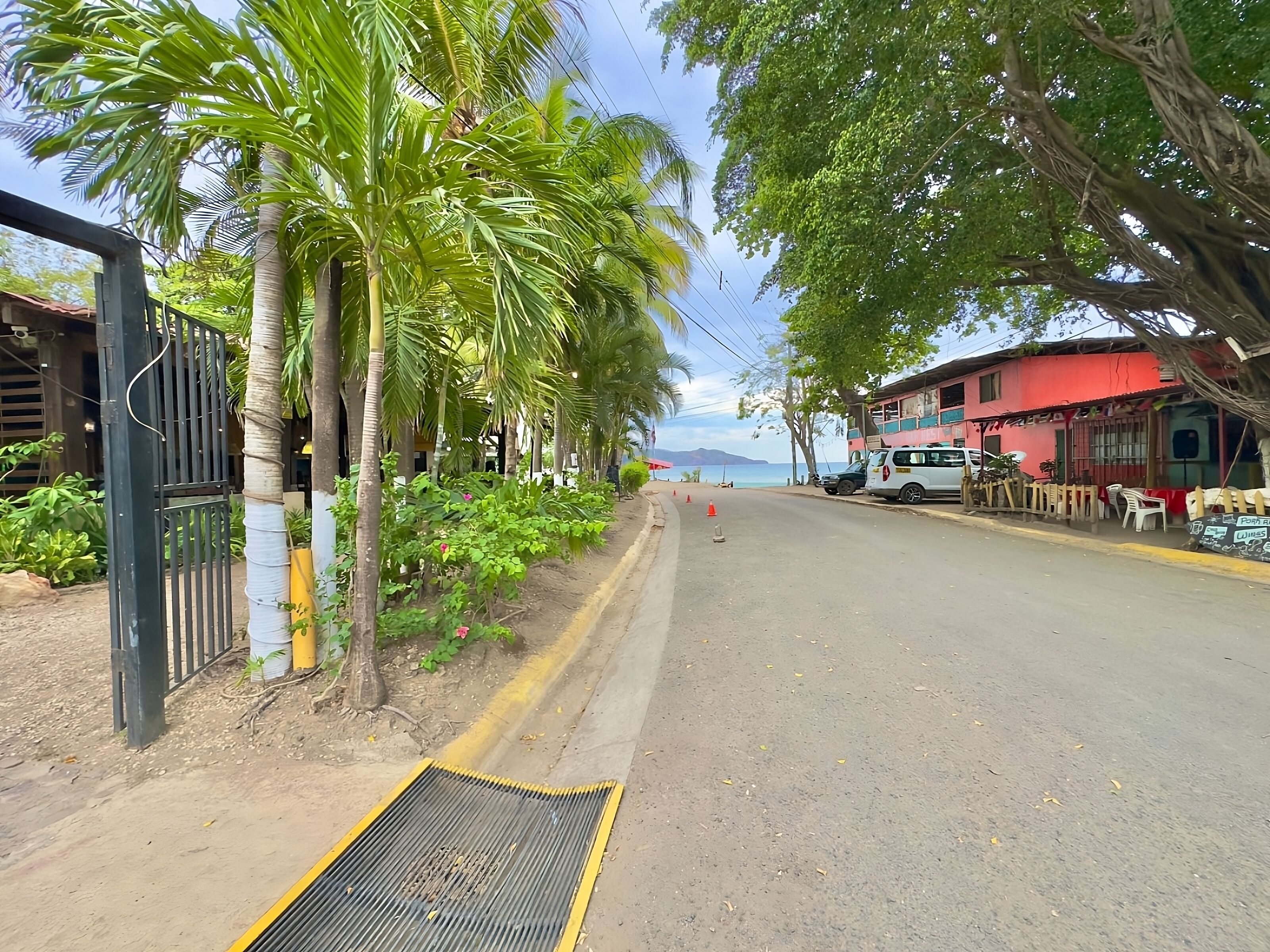 A street lined with palm trees and a red building with a visible entrance.
