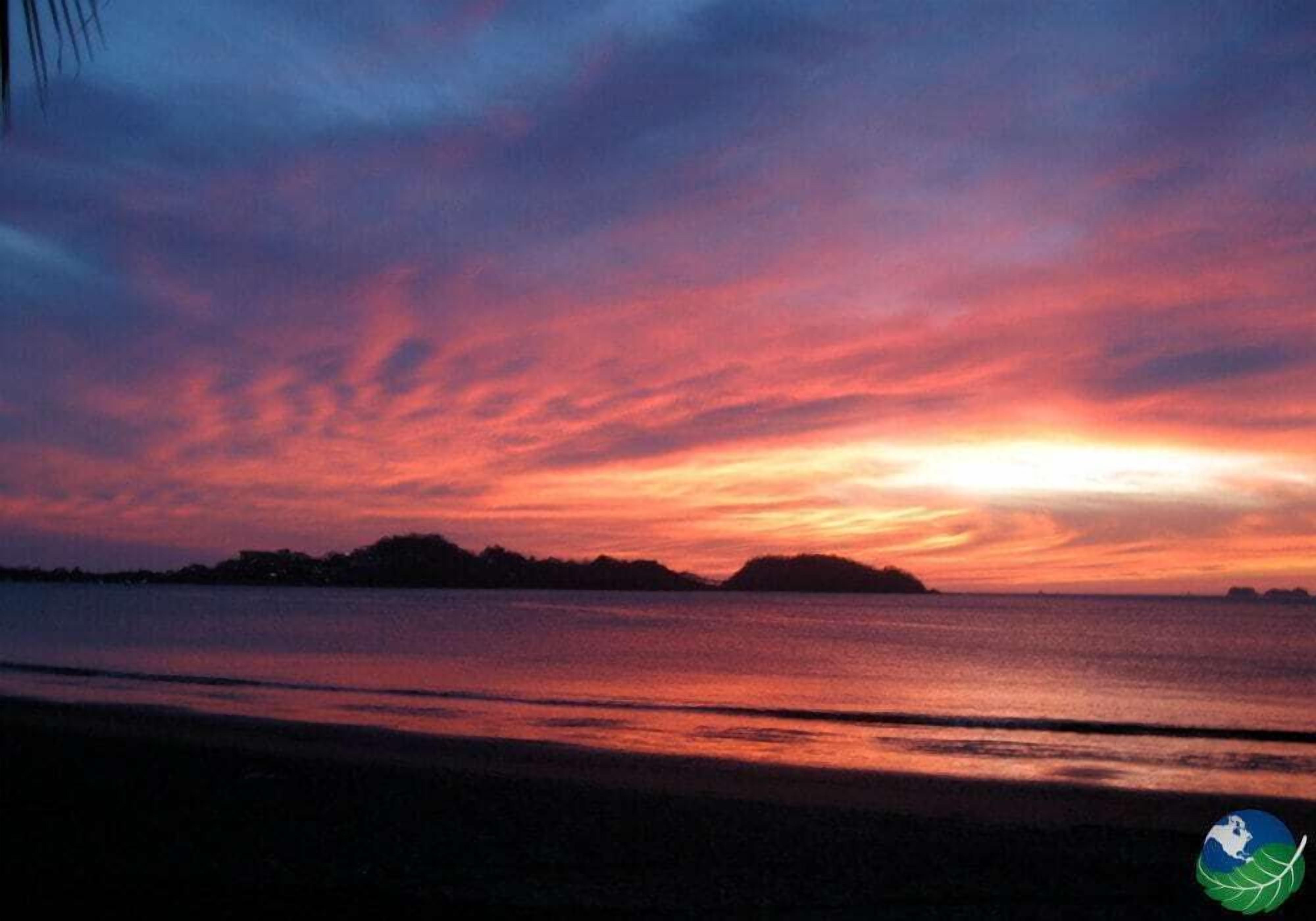 A sunset over a body of water with a silhouette of land in the distance.