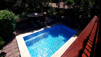 Una piscina rectangular con agua azul cristalina, rodeada por una terraza de madera y abundante vegetación.