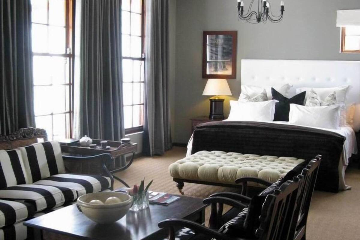 A hotel room with a large bed, a sofa, a dining table, and a chandelier.