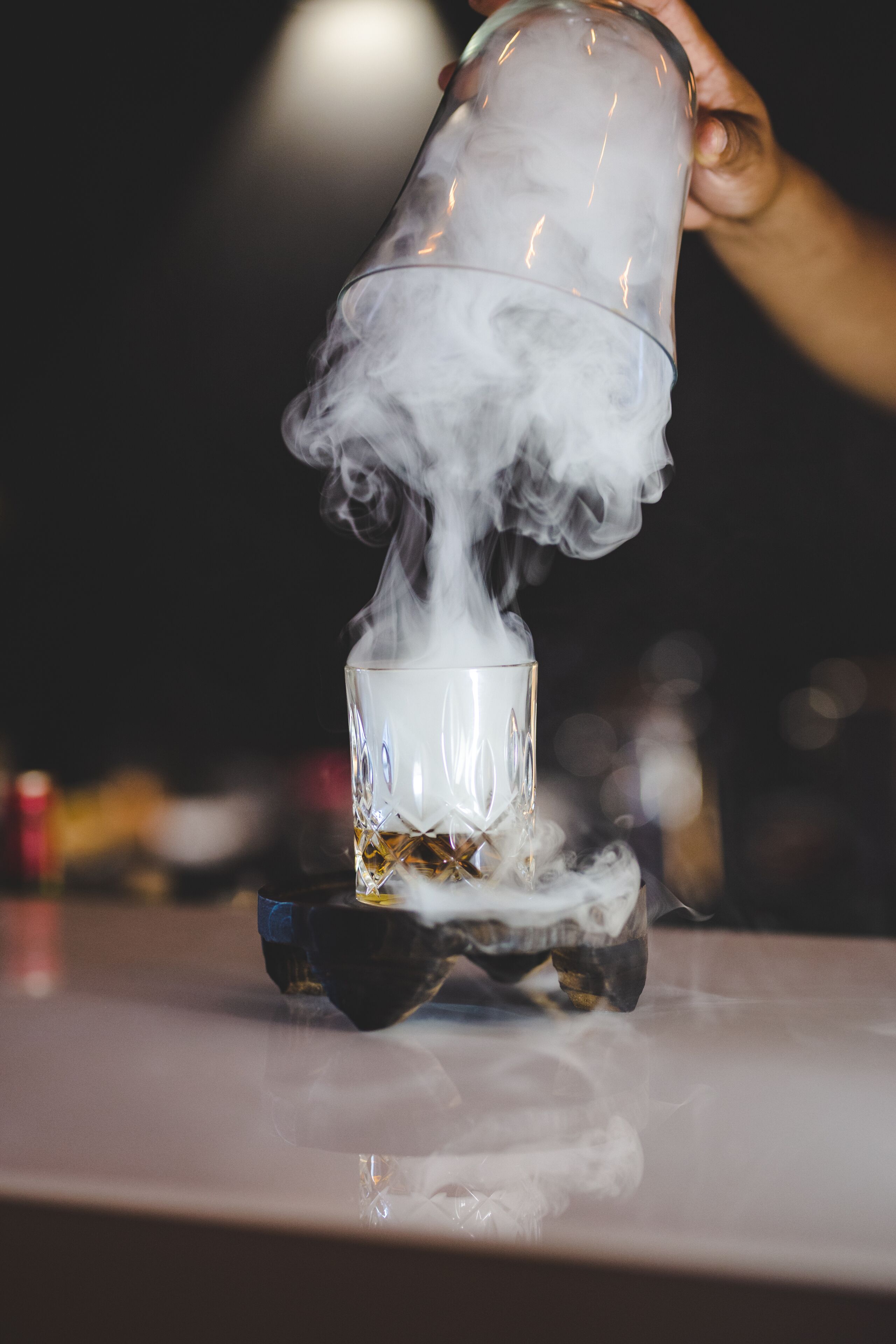 Une main verse un liquide transparent dans un verre, créant ainsi un effet fumé.