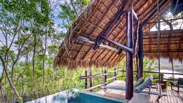Une piscine à débordement dotée d’une terrasse en bois et d’une structure surmontée d’un toit de chaume.