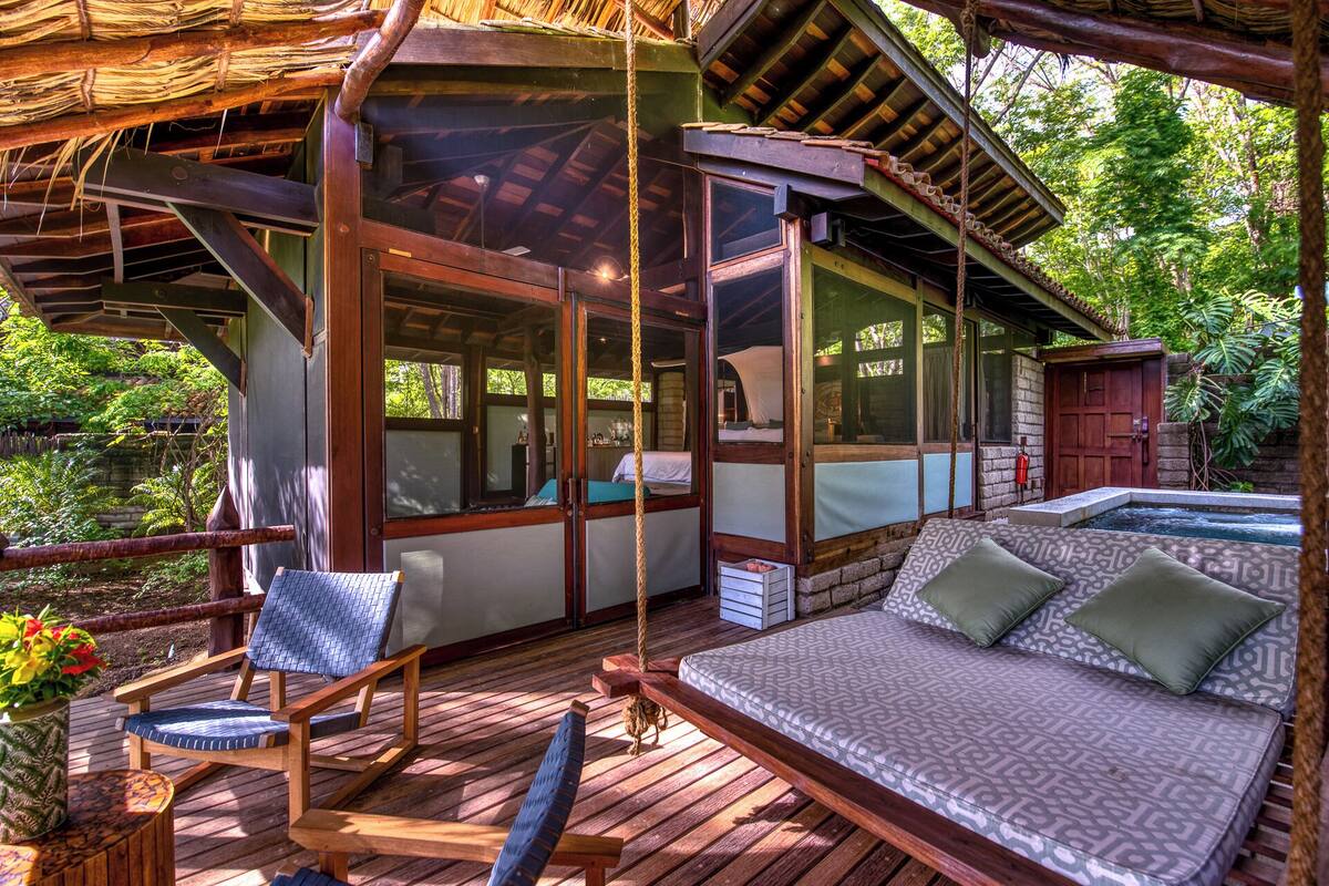 Terraza de madera con sofá y sillones, una piscina pequeña y una estructura de techo de paja.
