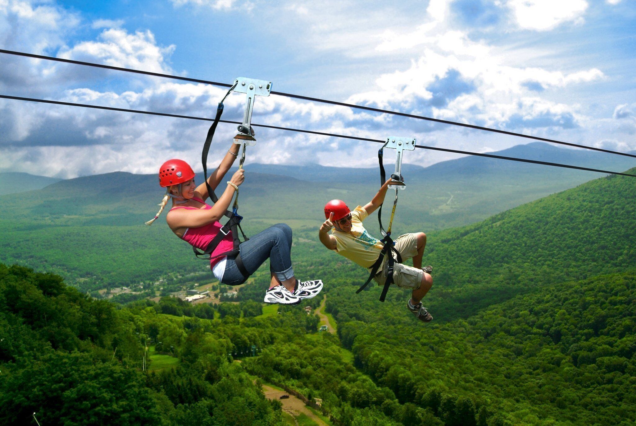 Twee personen zweven op een zipline boven een weelderig groen landschap.