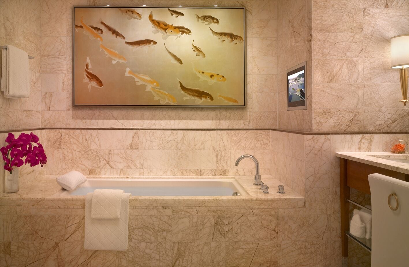 Un baño con un lavamanos de mármol, un gran mural de peces y un jarrón de orquídeas rosas.