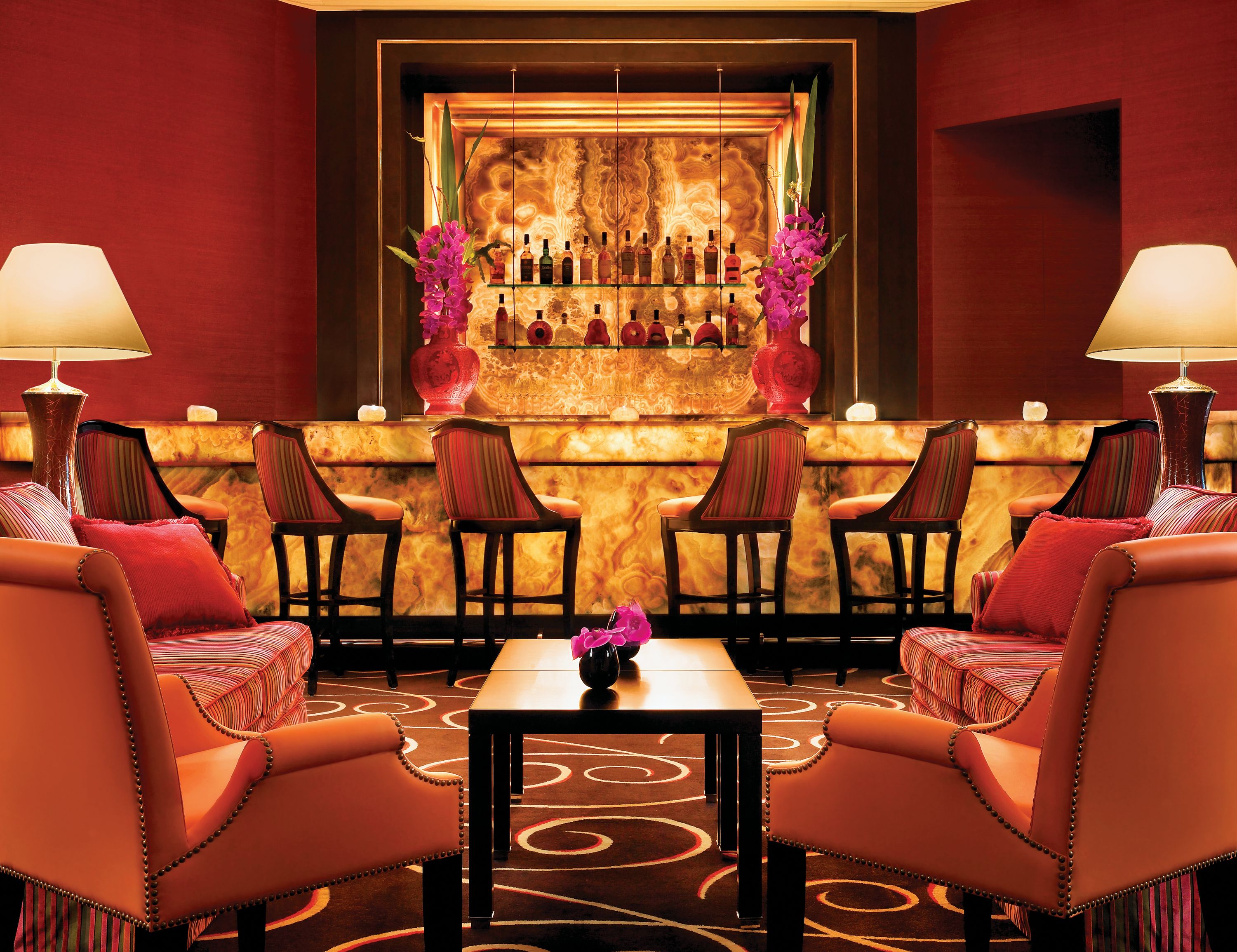 A bar area with leather chairs, a small table with a vase of flowers, and a shelf with bottles.