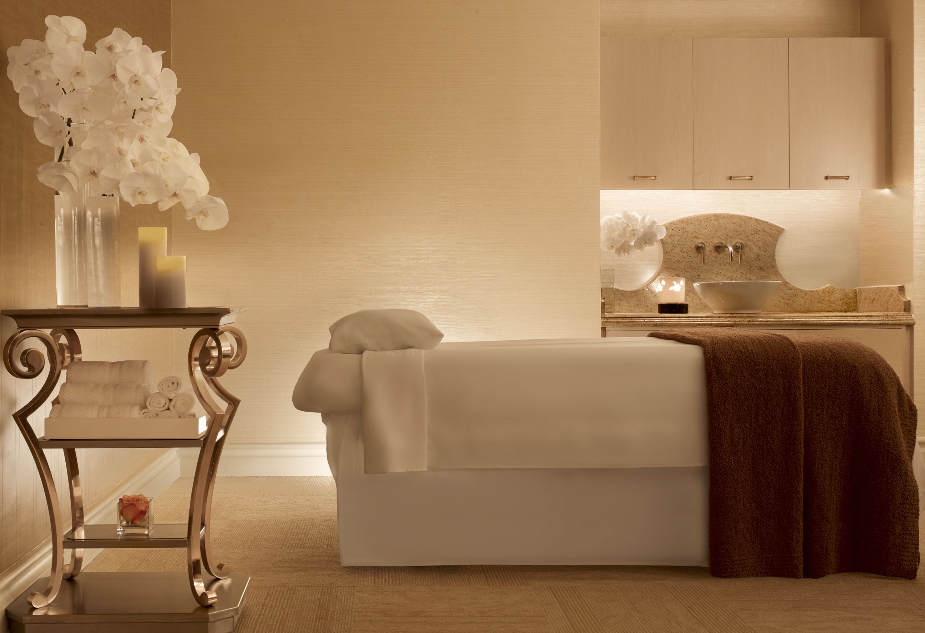 Un cuarto de spa con una cama, un tocador con un florero y un lavamanos al fondo.