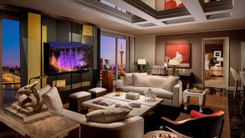 Habitación de hotel moderna con televisor grande, asientos cómodos, zona de comedor y vistas a la ciudad.