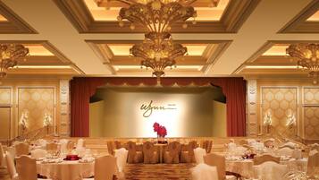 Une salle de banquet avec des tables rondes, des chaises blanches et une scène sur laquelle on peut lire l’inscription « W JUM MACAU ».