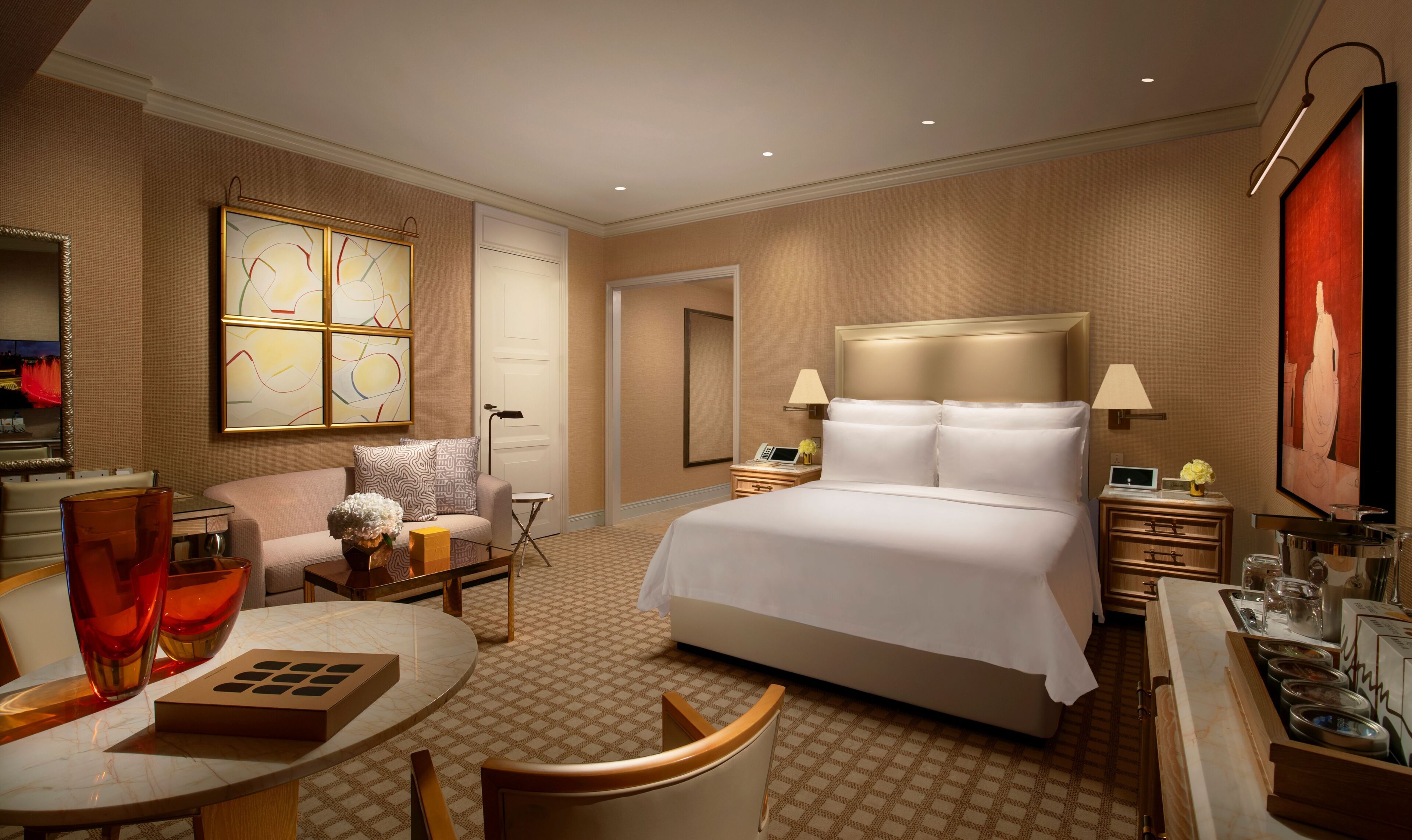 Ein Hotelzimmer mit Bett, Nachttischen, Schreibtisch, Stuhl, rundem Tisch und Kunstwerken an den Wänden.