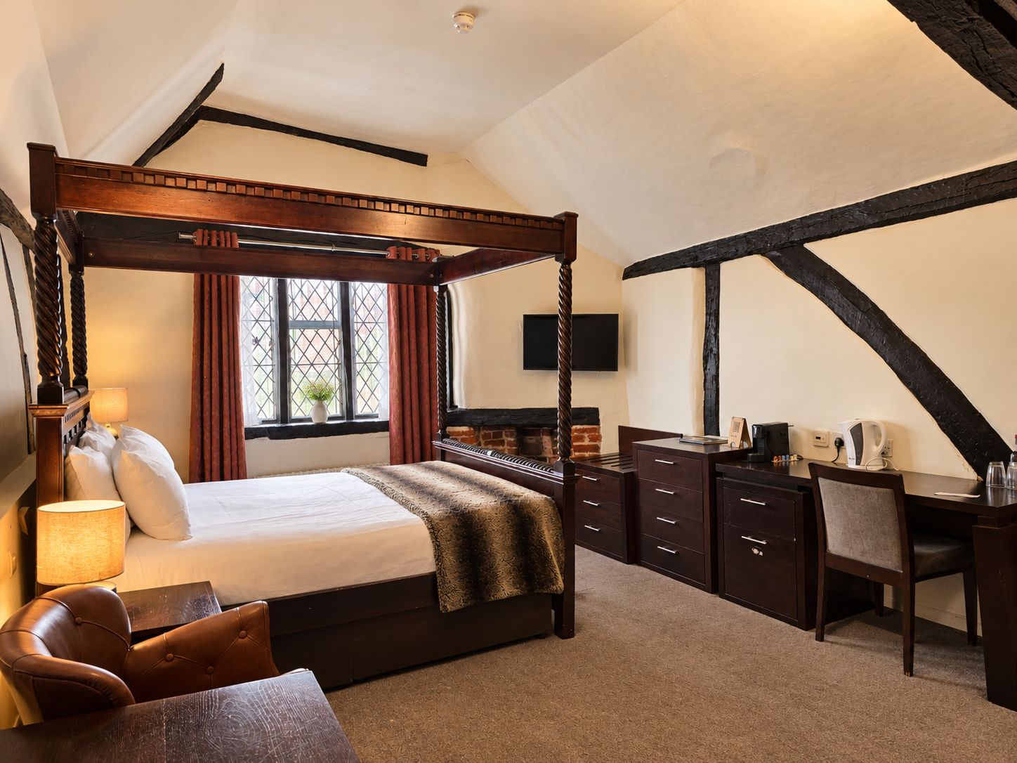 Ein Bett mit Himmelbett, ein Schreibtisch mit Schubladen, ein Stuhl und ein an der Wand befestigter Fernseher.