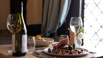 A dining table with a bottle of wine, two glasses, a plate of food, and a salt shaker.