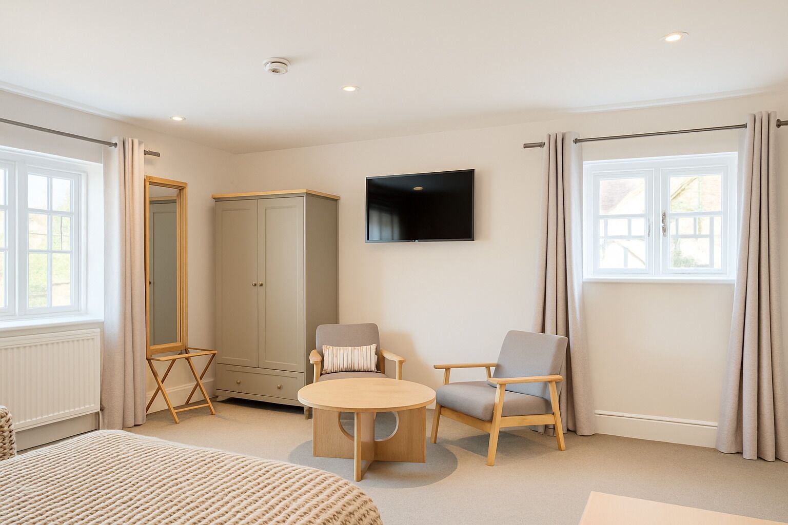 A room with a bed, a round table, two chairs, a wardrobe, a television, and large windows with curtains.