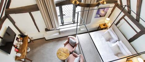 Une pièce aux hauts plafonds avec des poutres apparentes, une table en bois, deux fauteuils, un canapé et un luminaire suspendu.