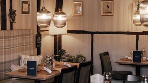 A restaurant with wooden beams, hanging pendant lights, and framed artwork on the walls. - The Kings Arms Hotel (Amersham)