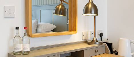 A wooden desk with a mirror, two lamps, and two bottles of alcohol.