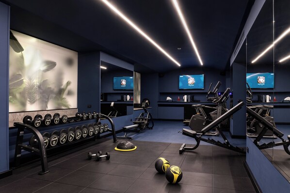 Un gimnasio con equipo de ejercicio, pesas y paredes espejadas.
