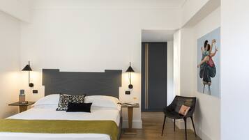 Une chambre d’hôtel moderne avec un grand lit, deux tables de chevet avec des lampes, une chaise et un tableau au mur.