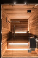 A sauna with wooden slats, a bench, a heater, and a small table with a bucket.