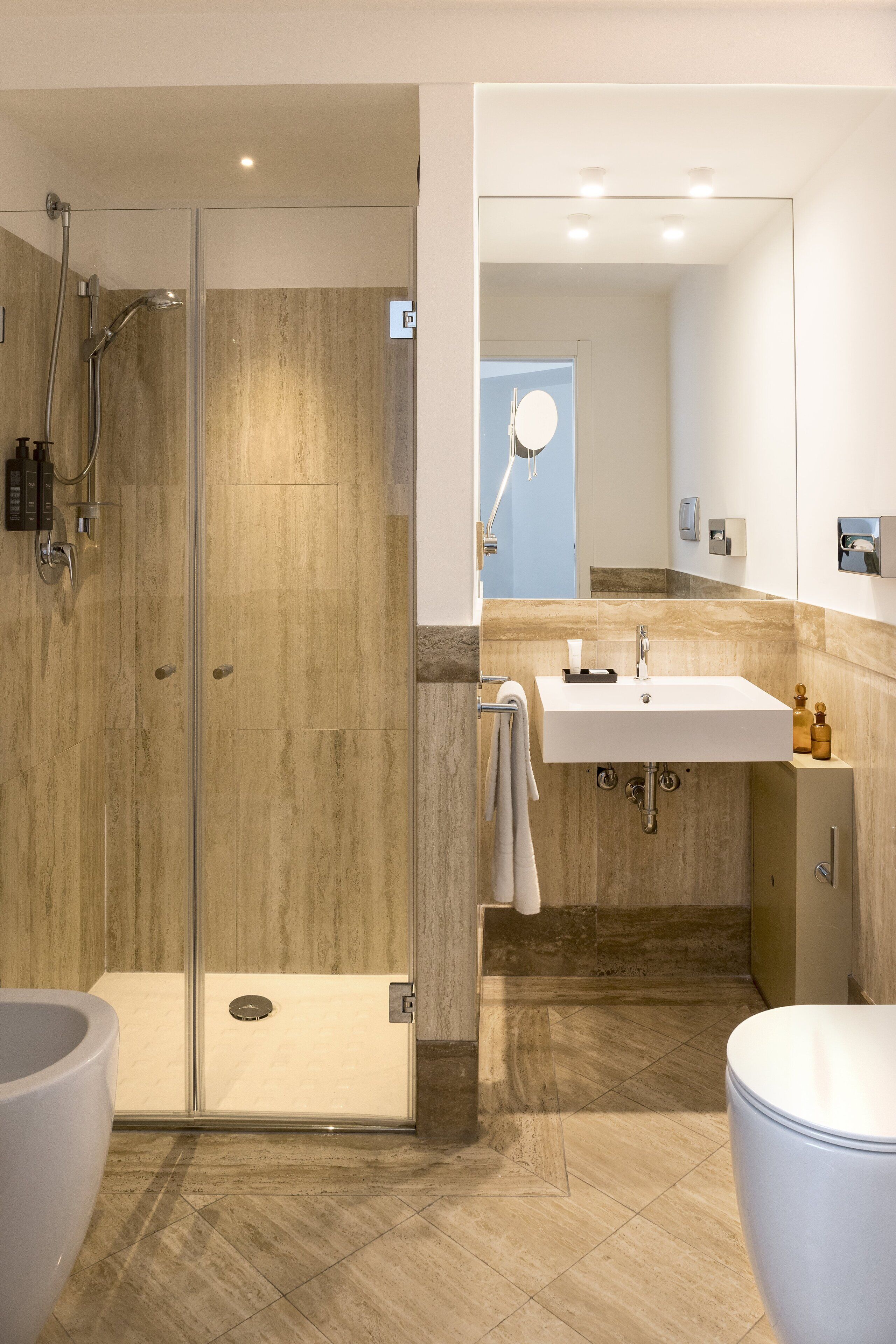 Un baño moderno con ducha envuelta en vidrio, lavabo blanco y suelo de mármol.
