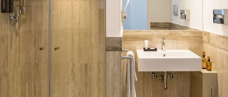 Un baño moderno con ducha envuelta en vidrio, lavabo blanco y suelo de mármol.
