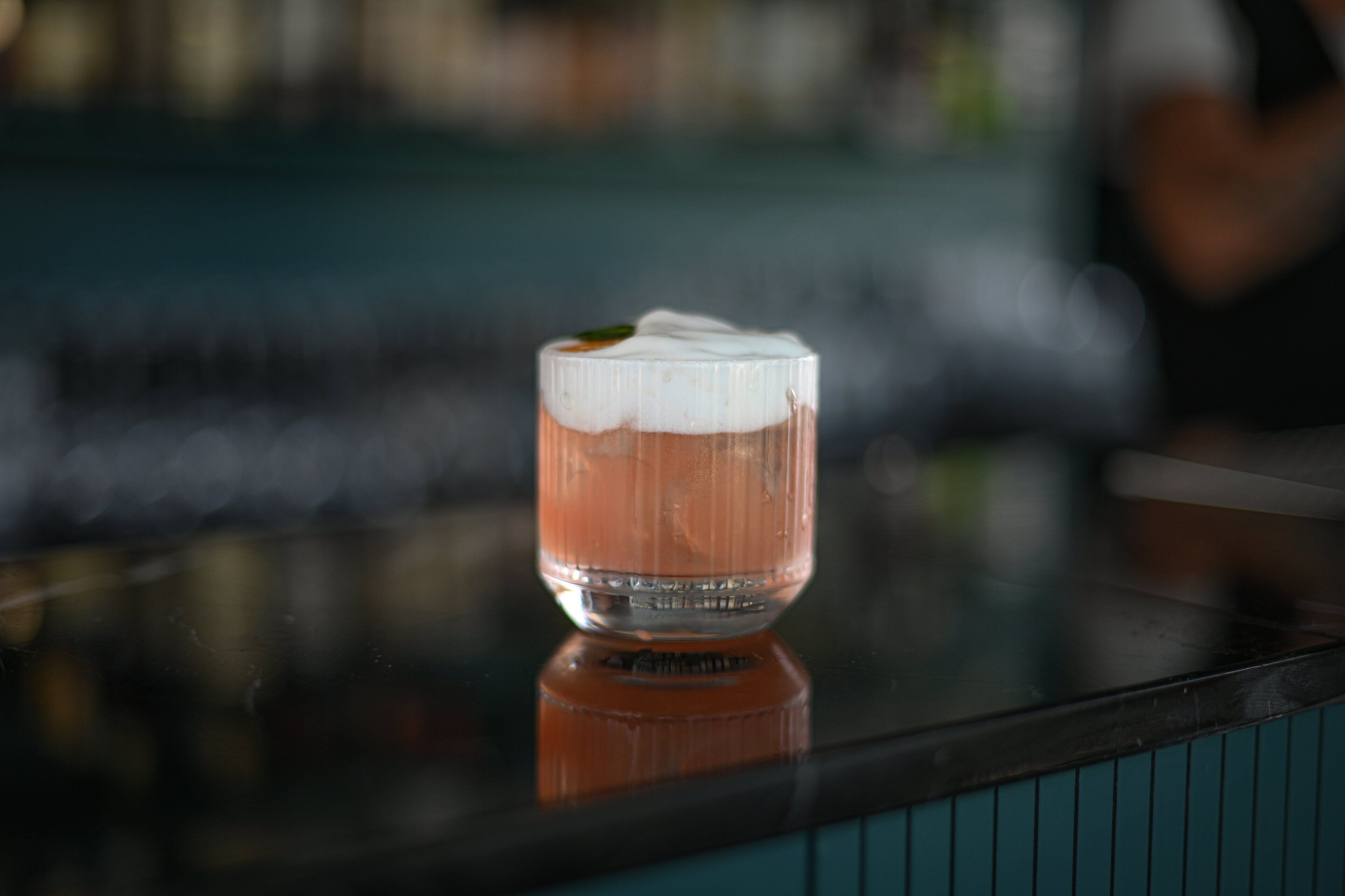 Un vaso de cóctel rosa sobre una superficie reflectante.