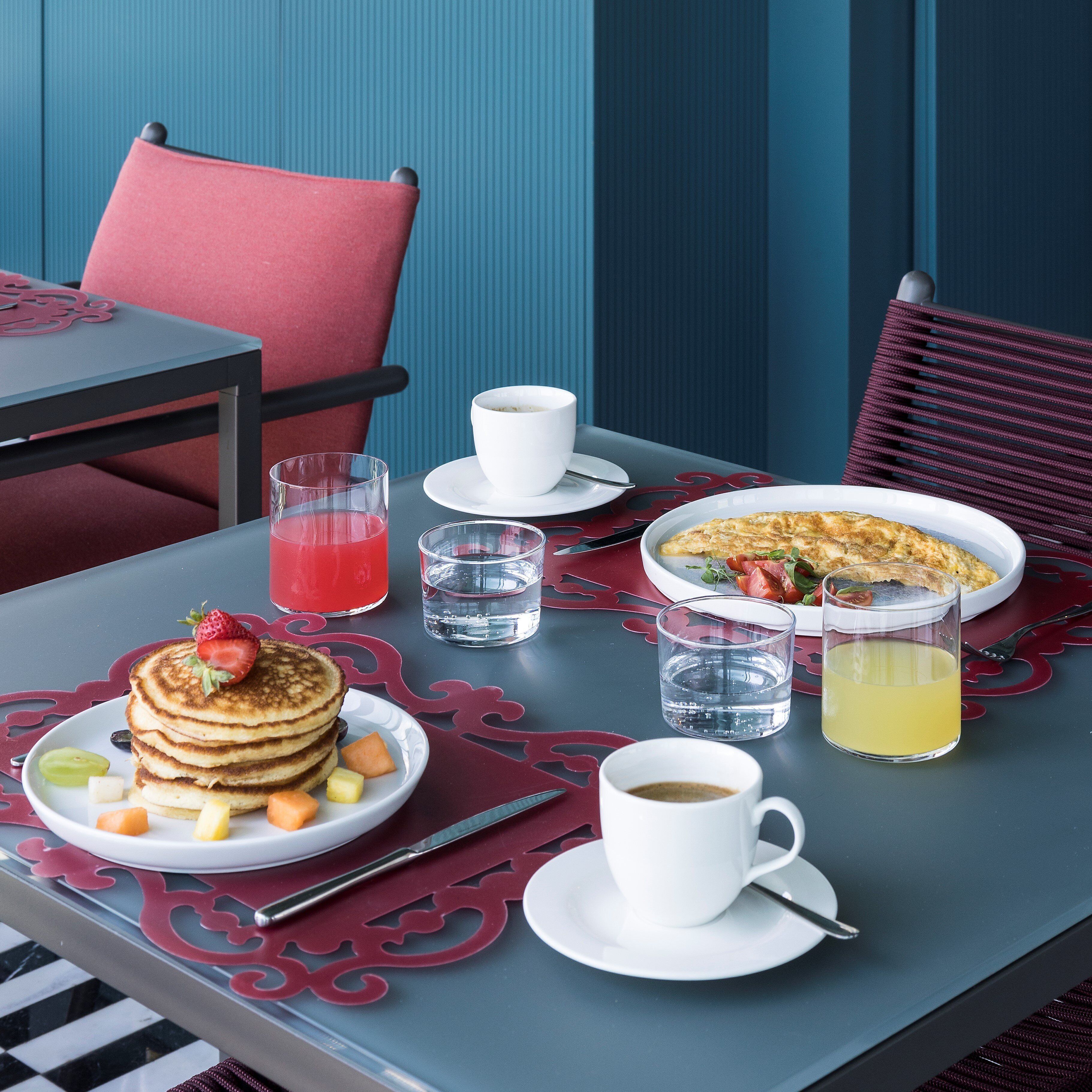 A breakfast table with pancakes, fruit, coffee, and a glass of orange juice.