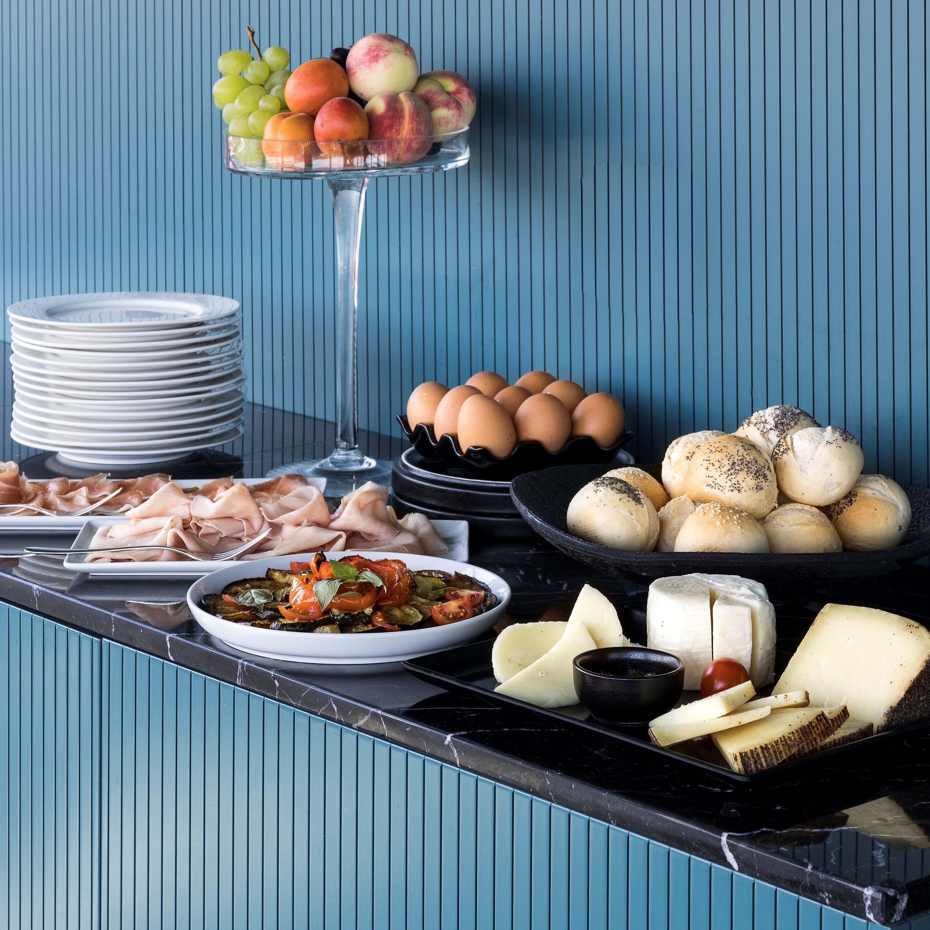 Una mesa de buffet con diversos alimentos como frutas, huevos, carnes, quesos y pan.