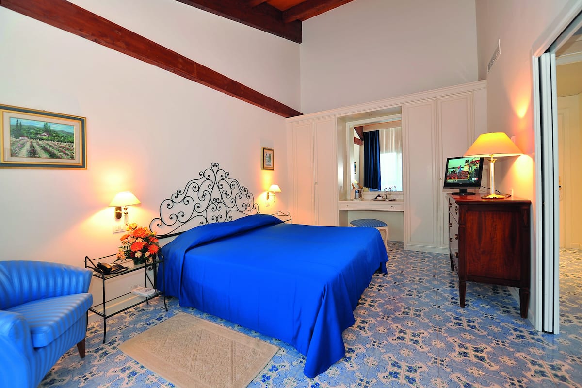 A bedroom with a large bed, two bedside tables with lamps, a chair, a dresser, and a mirror.