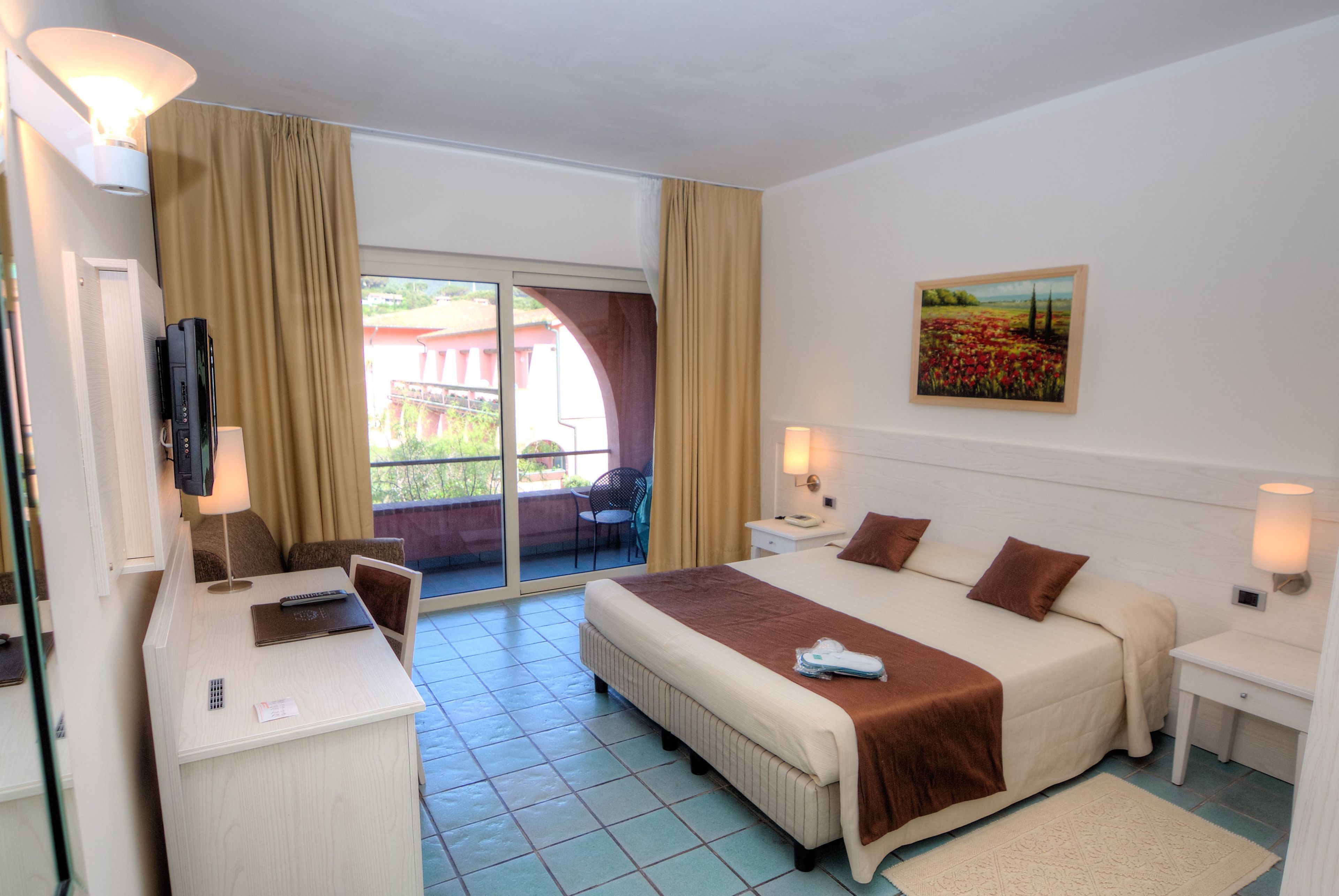 A hotel room with a bed, a desk, a chair, a TV, a painting, and a balcony.