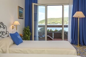 A bedroom with a bed, two wall-mounted lamps, a window with a view of a balcony, and a painting on the wall.