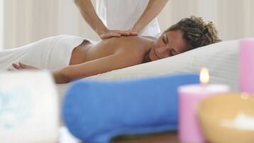 Eine Massagebehandlung in einem Raum mit Liege, Kissen und Kerzen.