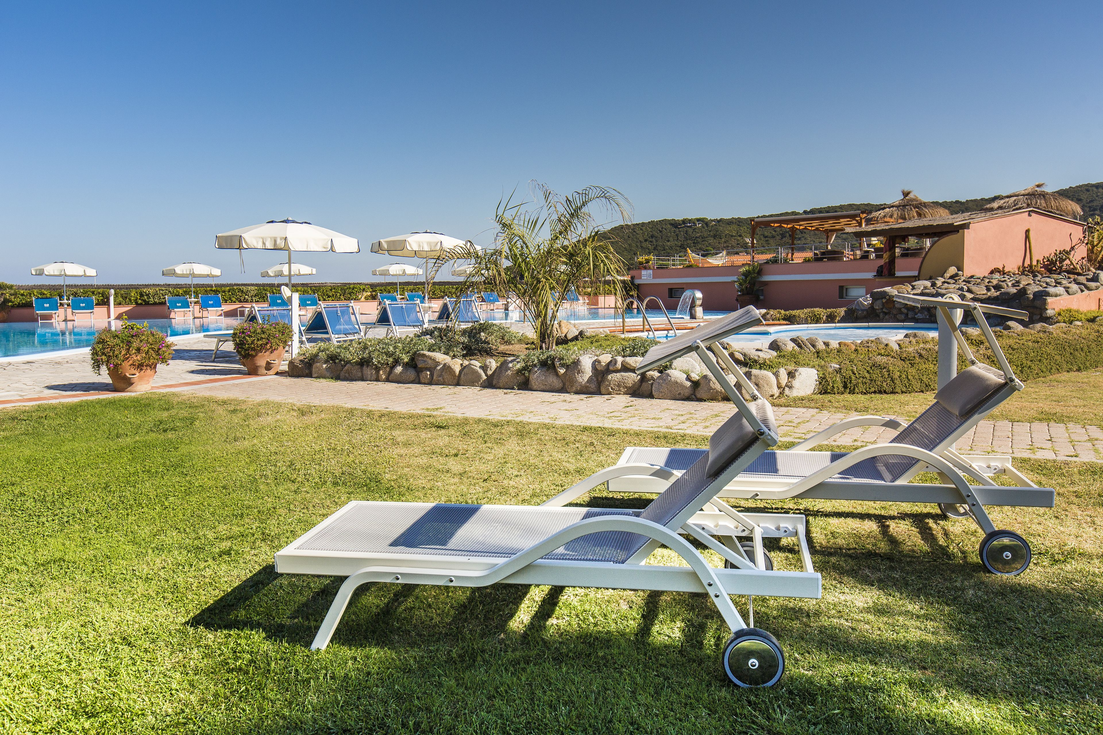 Un espace aménagé au bord de la piscine, avec des chaises longues et des parasols, un ciel dégagé et un bâtiment en arrière-plan.