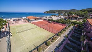 Una cancha de tenis con red, rodeada de edificios y vista al mar.