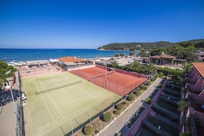 A tennis court with a net, surrounded by buildings and a view of the sea. - Hotel Del Golfo (Marciana)