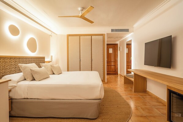 Un dormitorio moderno con una cama grande, ventilador de techo, televisor y chimenea.