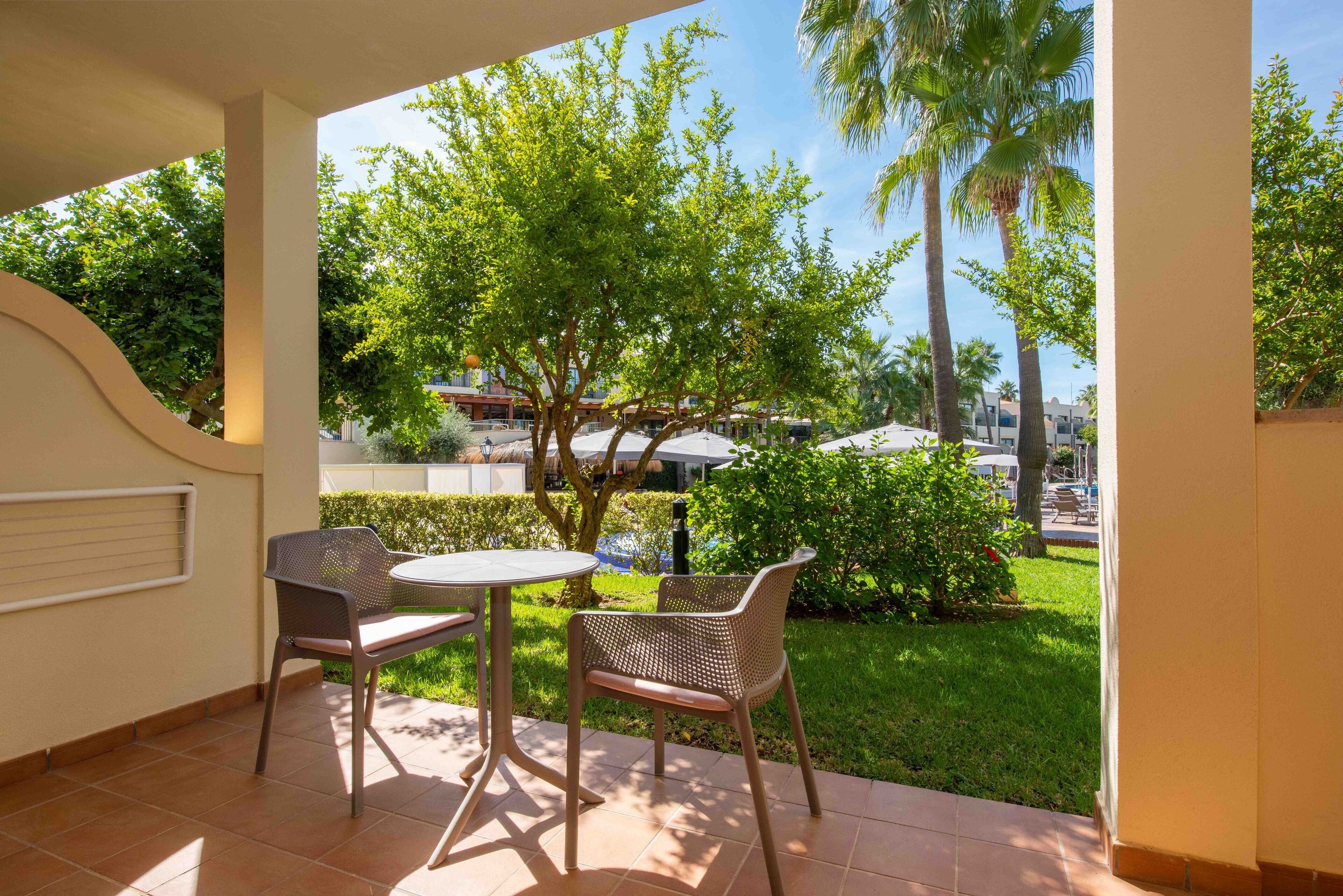 A patio with two wicker chairs and a small round table, overlooking a well-maintained garden with trees and a clear view of the surrounding area.