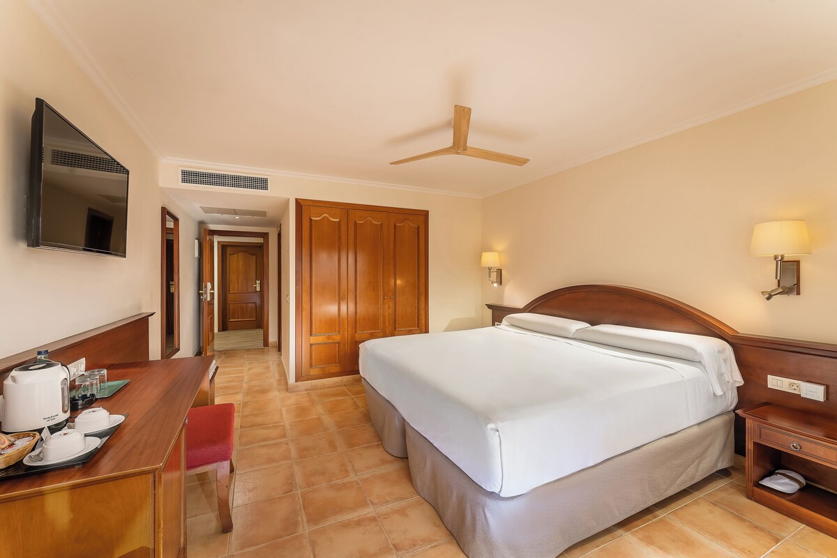 Une chambre d’hôtel équipée d’un lit, d’une table de chevet, d’une lampe et d’un bureau avec une bouilloire et des tasses.