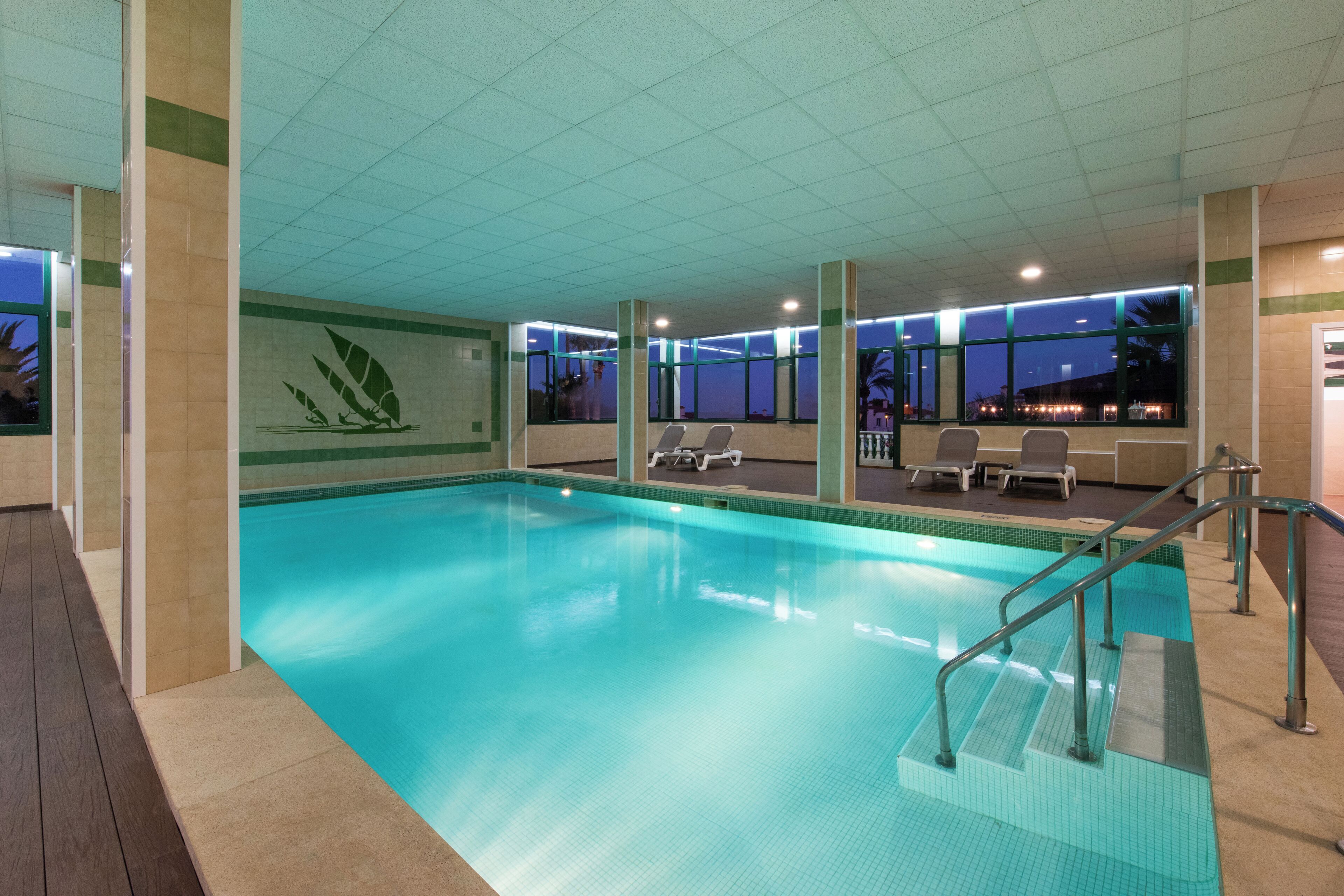 An indoor swimming pool with clear water, surrounded by lounge chairs and a tiled floor.