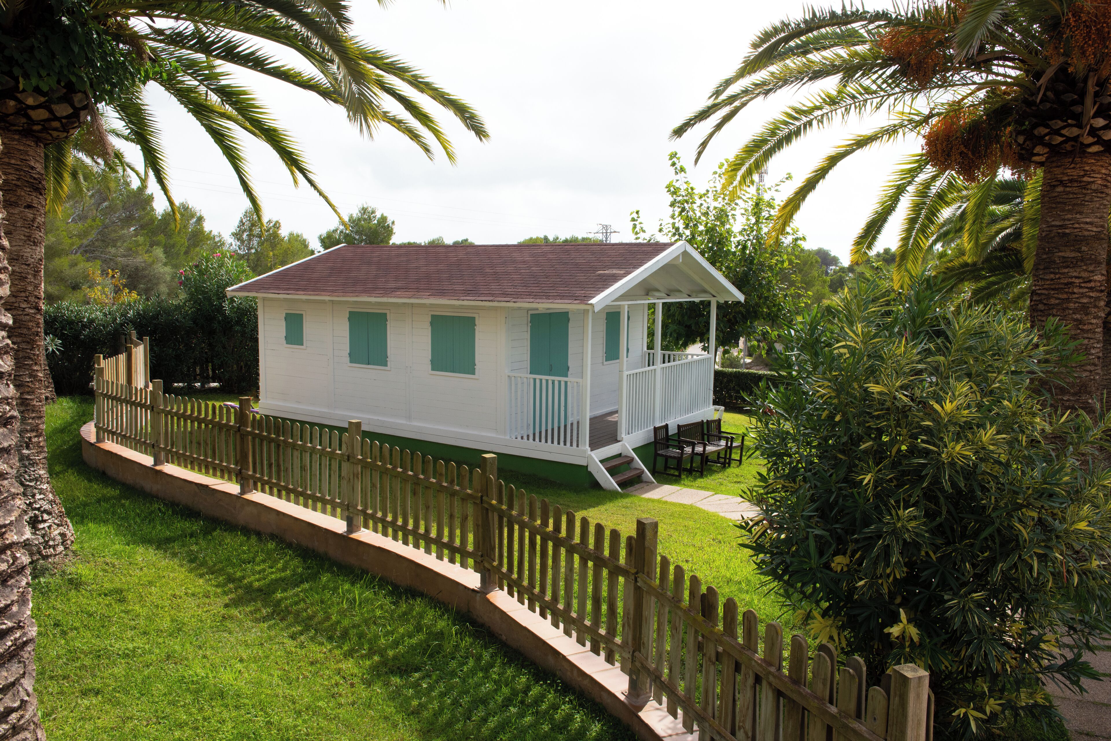 A white house with green shutters, a porch, and a wooden fence.