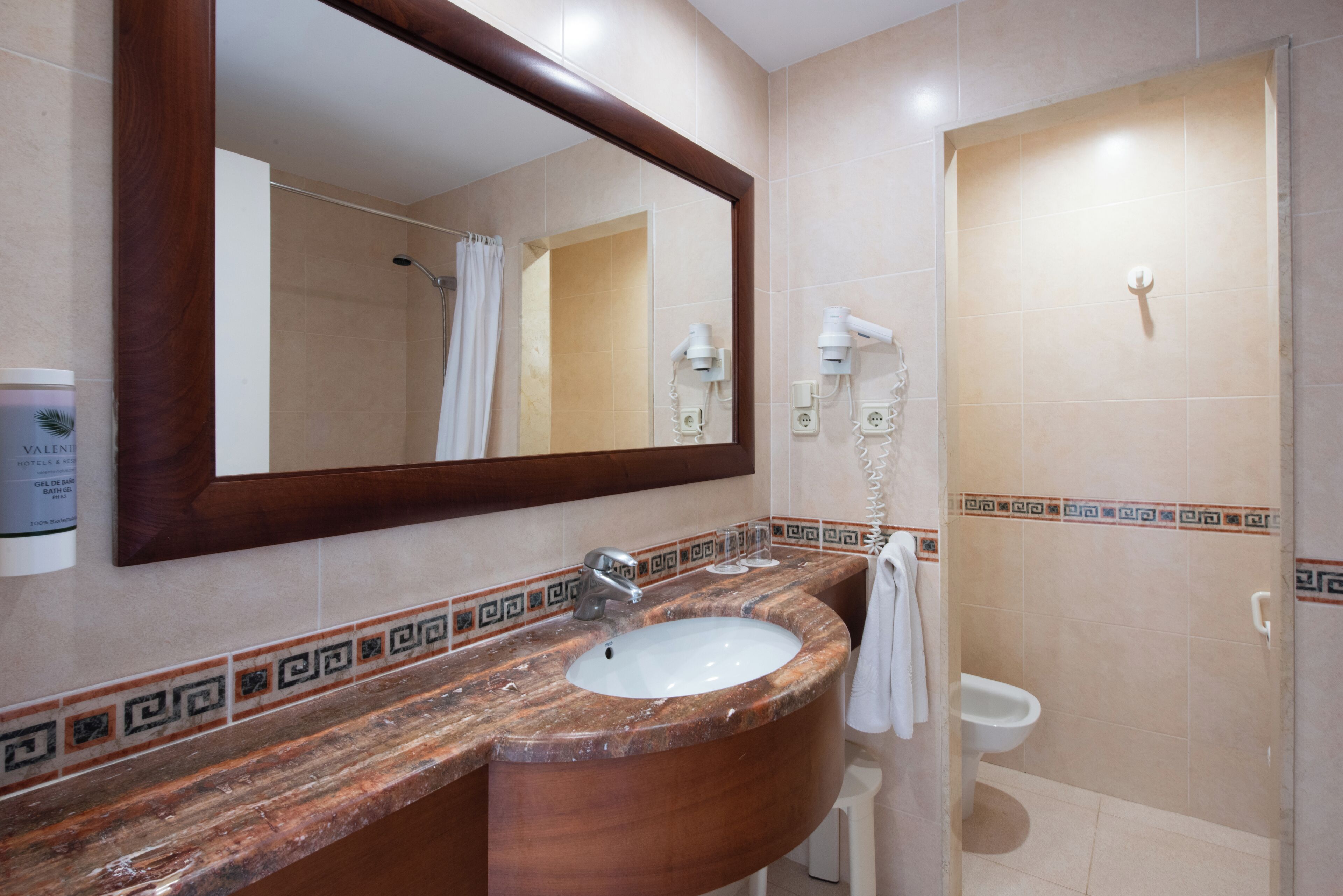 A bathroom with a marble sink, a large mirror, a shower, and a toilet.