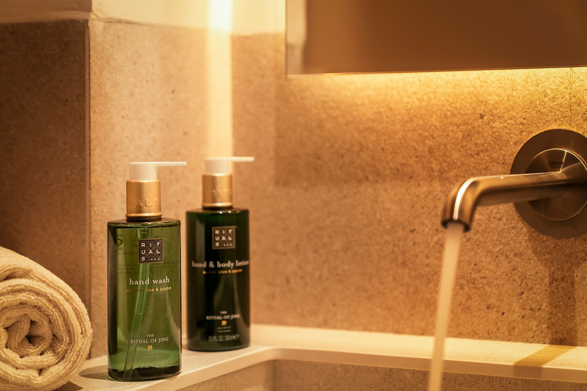A bathroom with a towel, two bottles of hand wash, and a shower head.