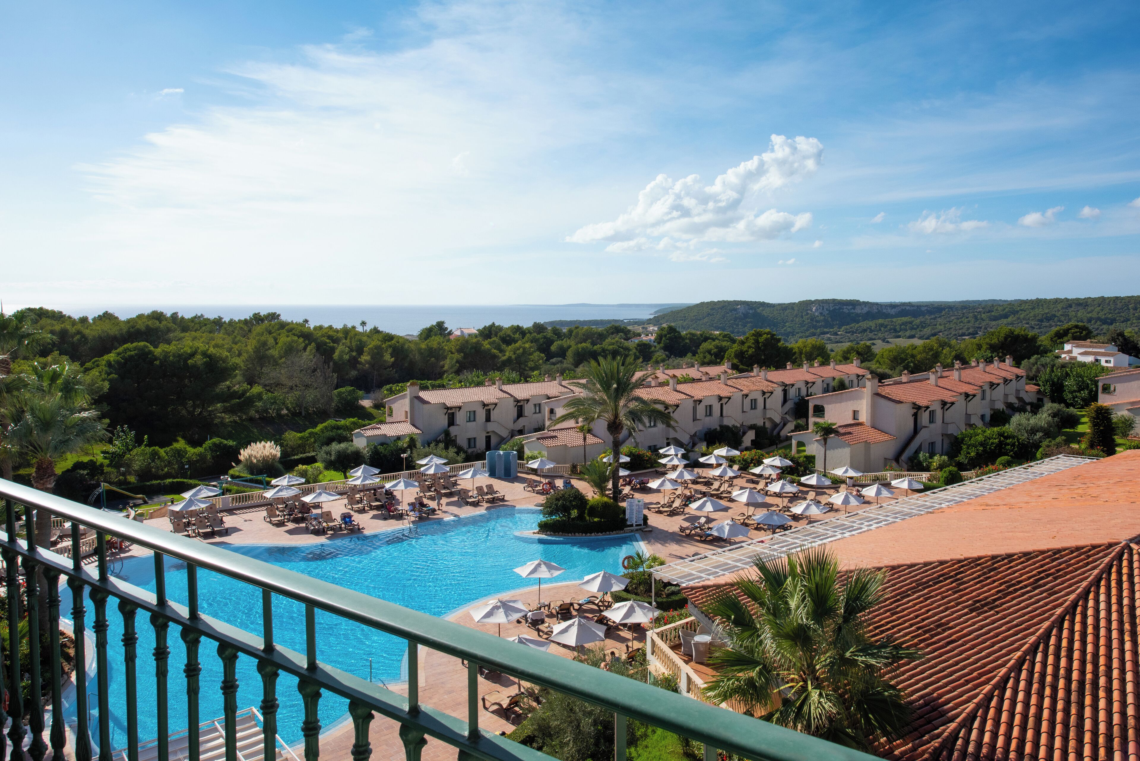 Un resort con una amplia piscina, varias zonas de descanso y vistas del paisaje circundante.