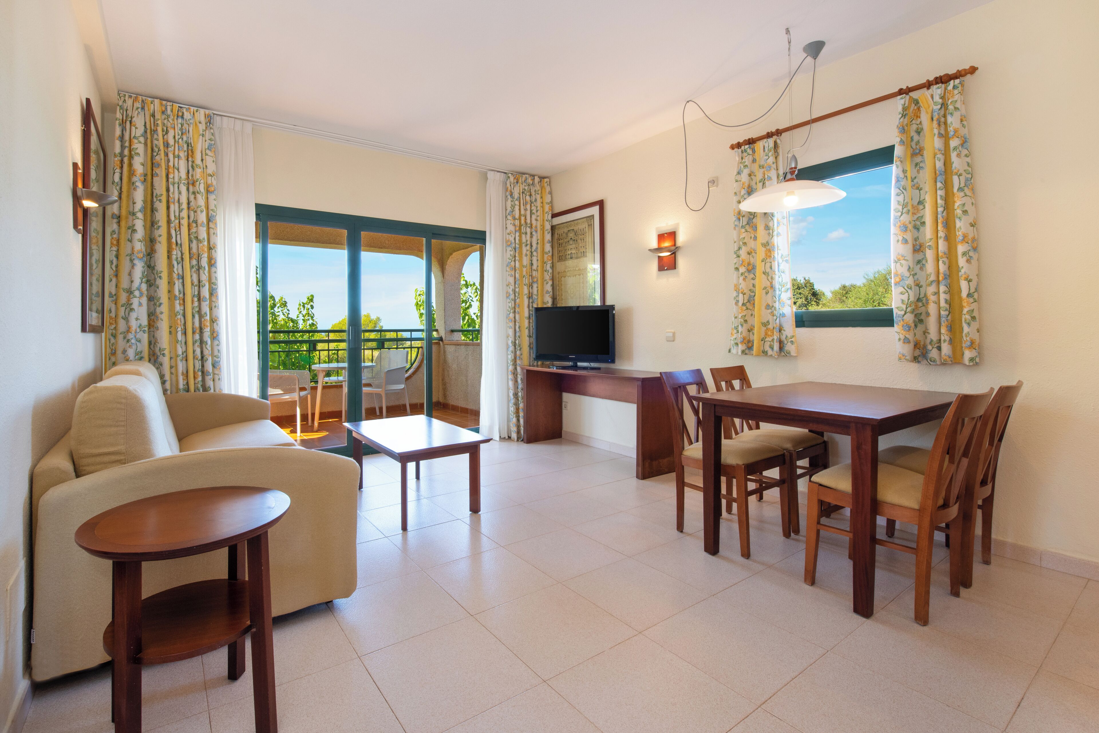 A living room with a sofa, coffee table, TV, dining table, chairs, and a balcony with curtains.