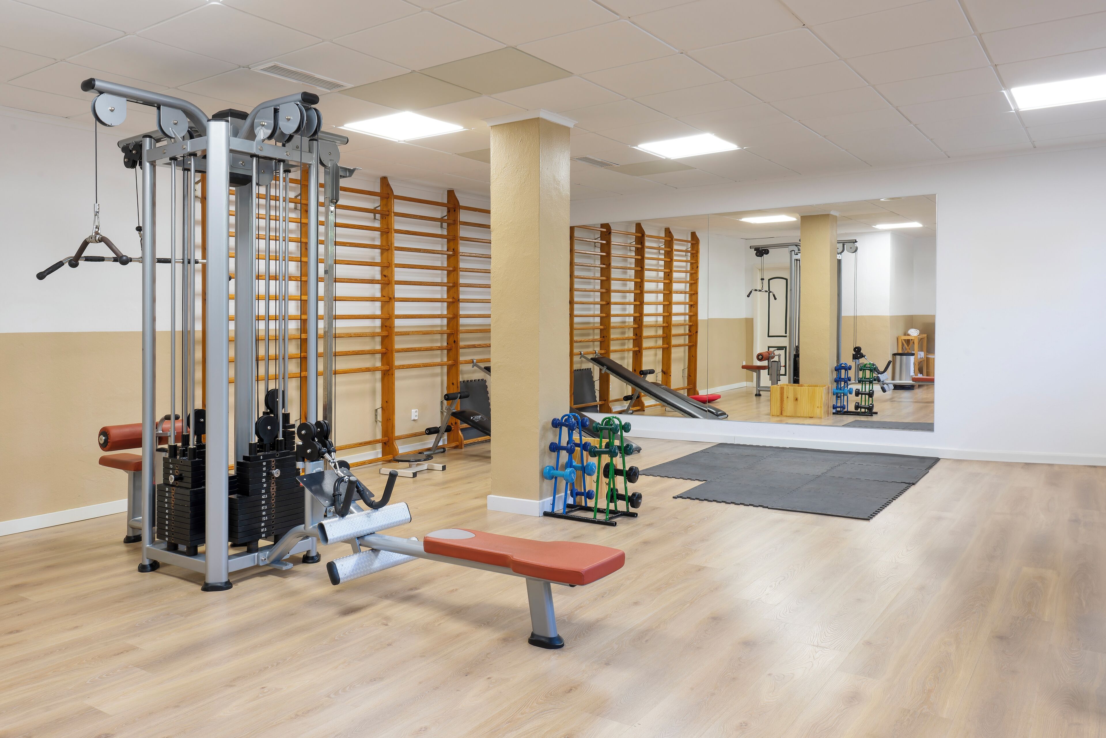 Uma academia com diversos equipamentos de exercícios, incluindo supino, aparelhos de musculação e pesos livres.