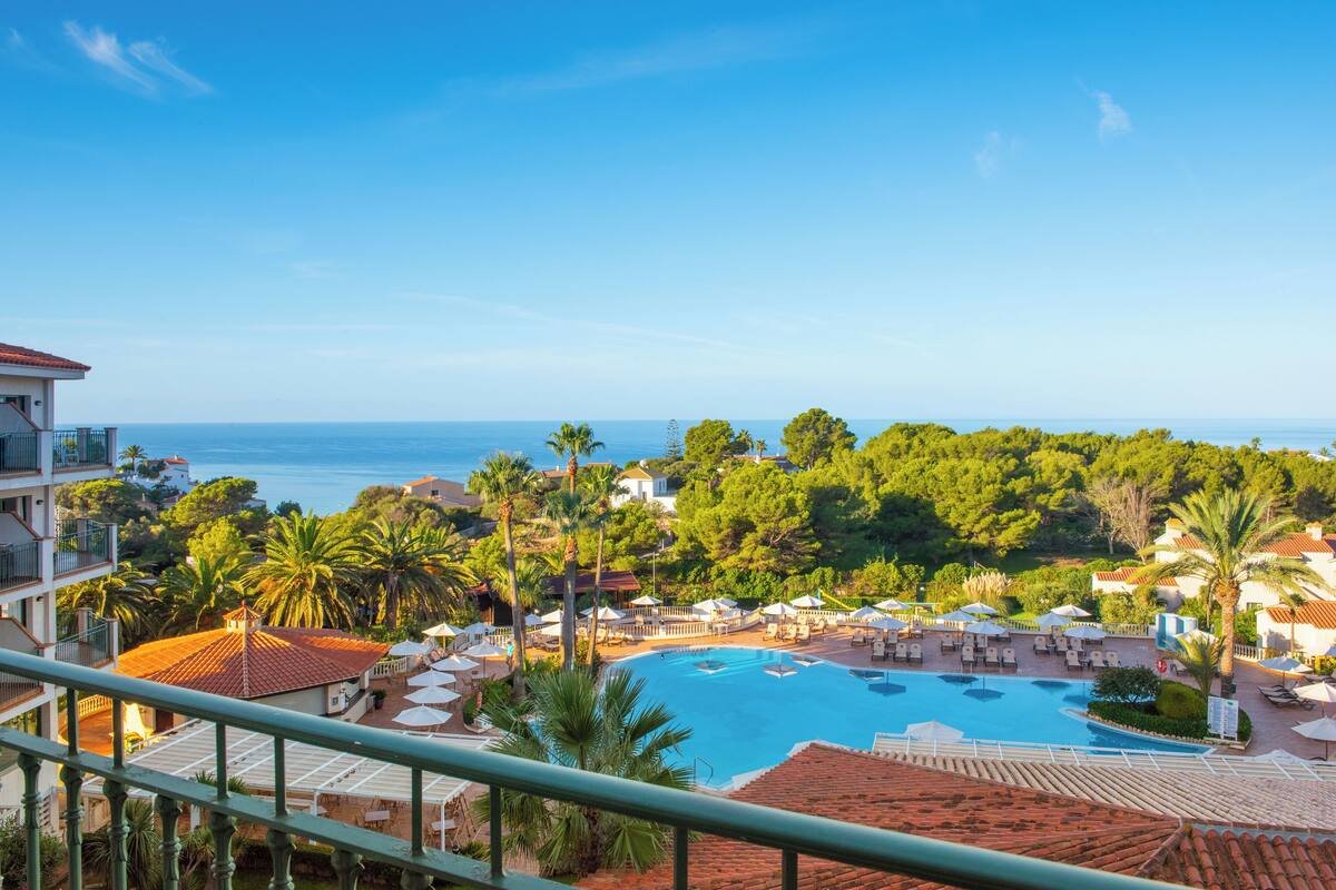 A resort with a large swimming pool, lounge areas, and a view of the sea.