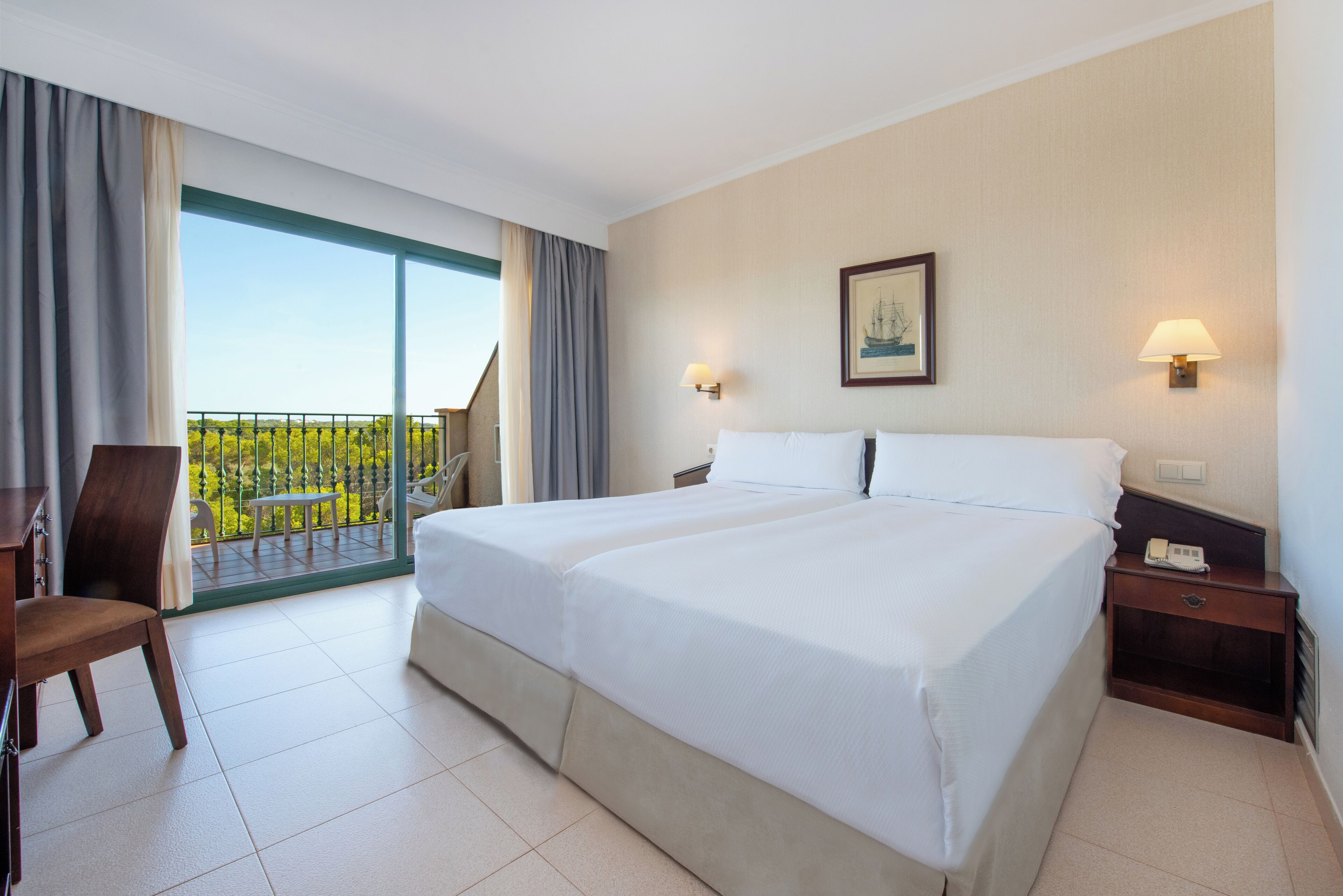 Habitación de hotel con una cama grande, un escritorio y una silla. Posee un balcón con vistas a zonas verdes.