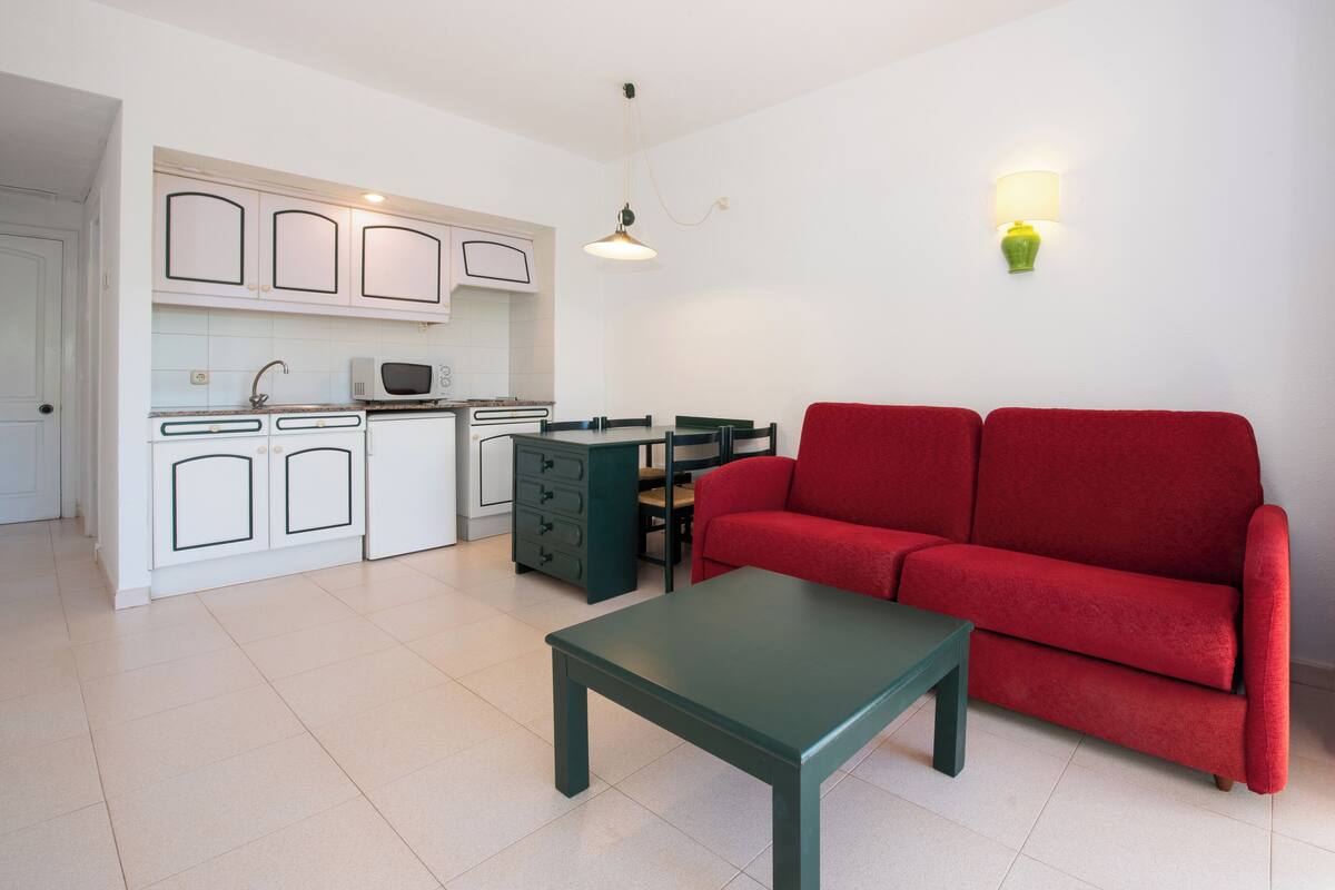 A compact living space with a kitchenette, a red sofa, and a green table.